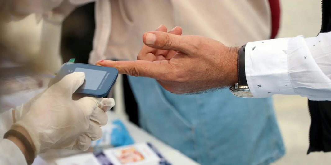 A healthcare worker in gloves takes a blood sugar reading from a man's fingertip using a handheld glucose meter