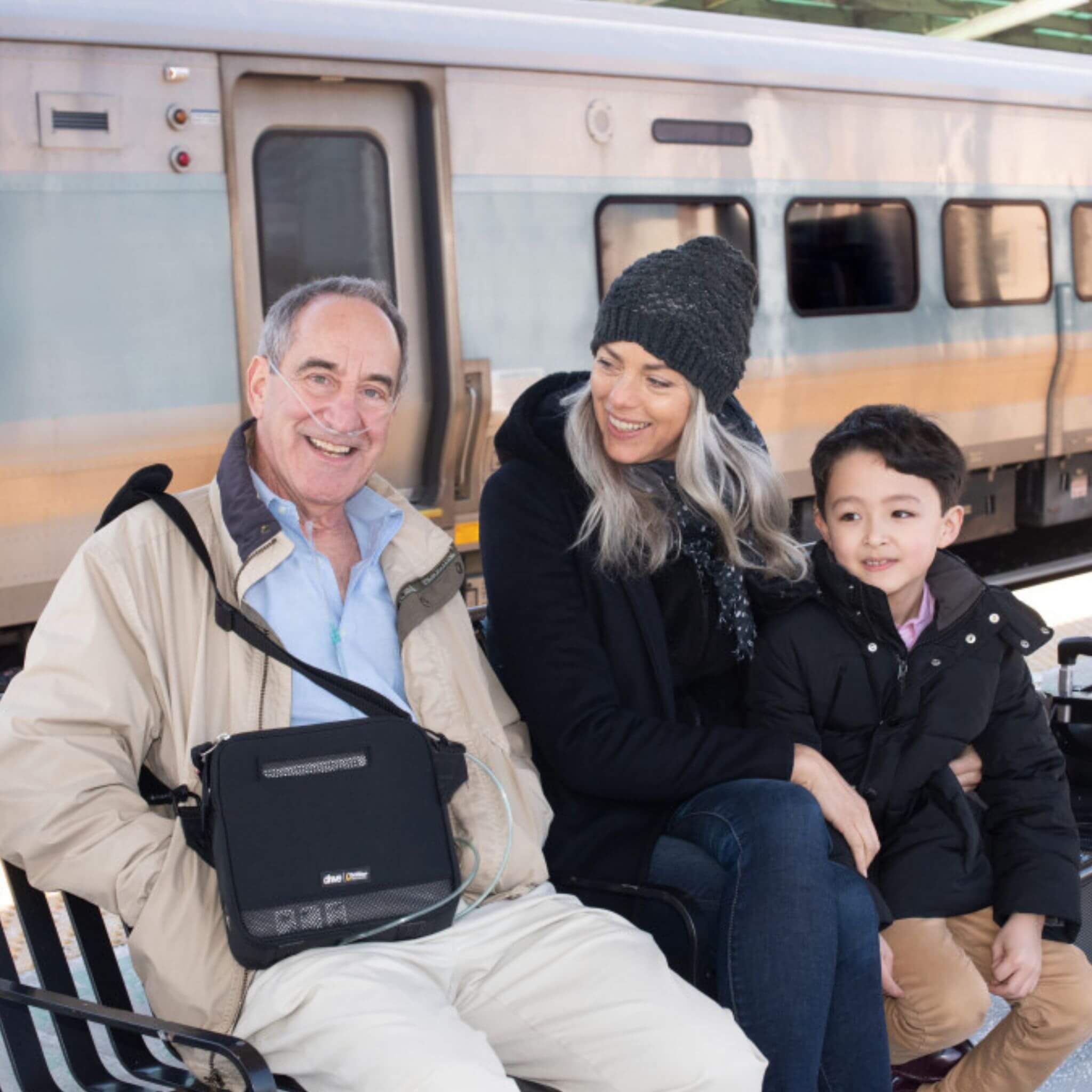 A man at railway station with family  and Devilbiss iGO2 Portable Oxygen Concentrator attached