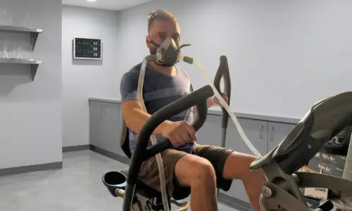 Person exercising with oxygen therapy on a bike with an oxygen mask in a room with