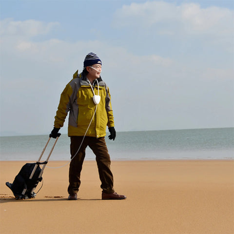 Person in yellow jacket with a portable oxygen concentrator on a sandy beach